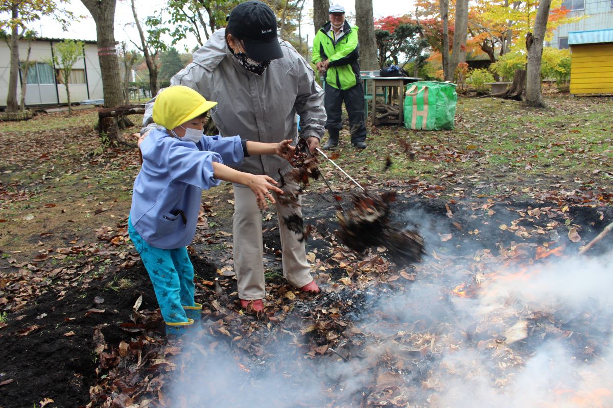 焼き芋用の火に落ち葉を投げ入れる5才児の様子